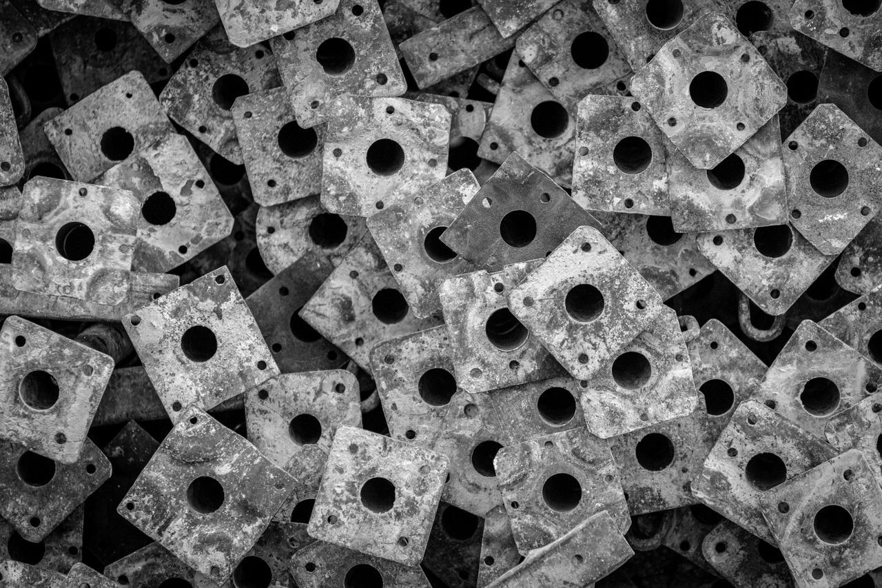 A close-up abstract composition of stacked, perforated metal plates in black and white, showcasing texture and pattern.